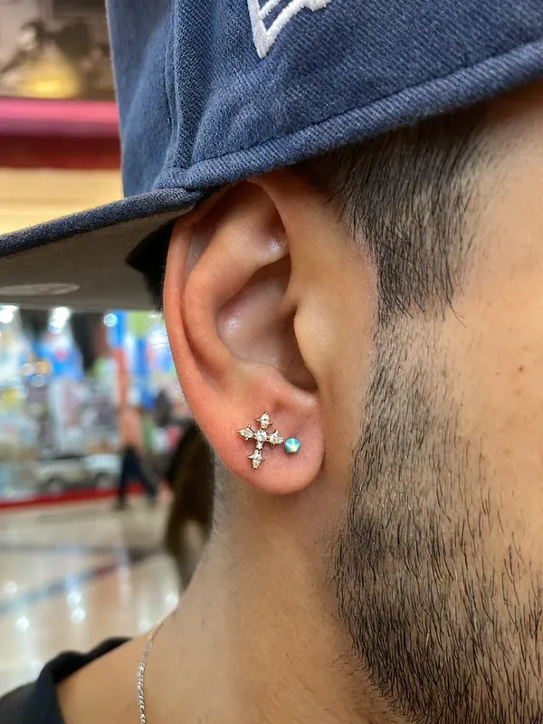 Piercing no lóbulo masculino com joia de cruz cravejada