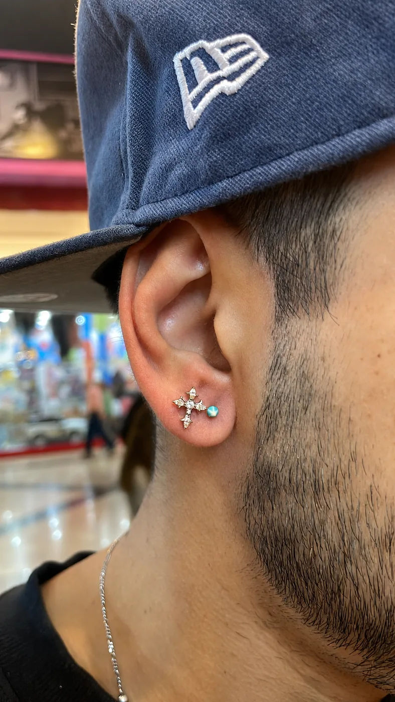 Piercing no lóbulo masculino com joia de cruz cravejada
