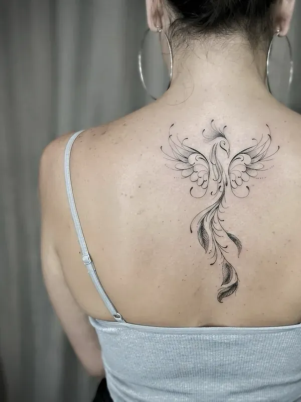 Tatuagem fine line de fênix entre as omoplatas