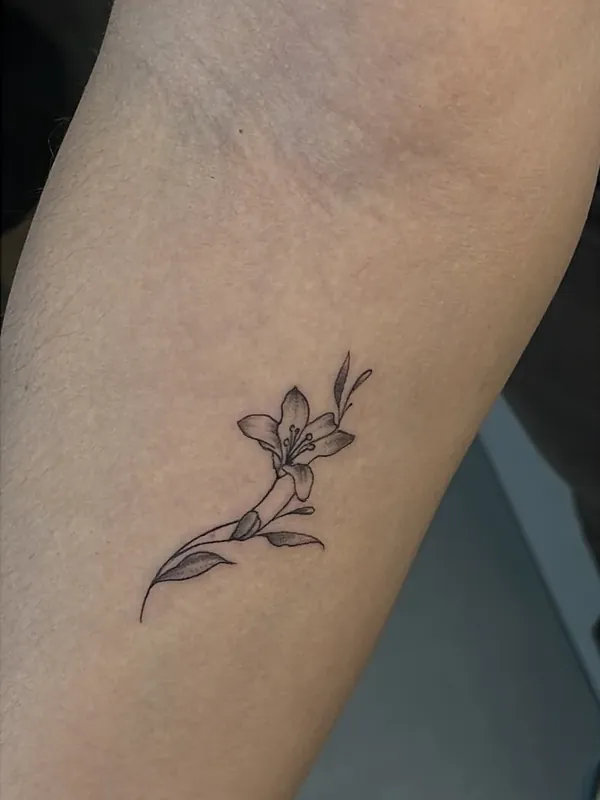 Tatuagem fine line pequena de lírio com folhas no antebraço