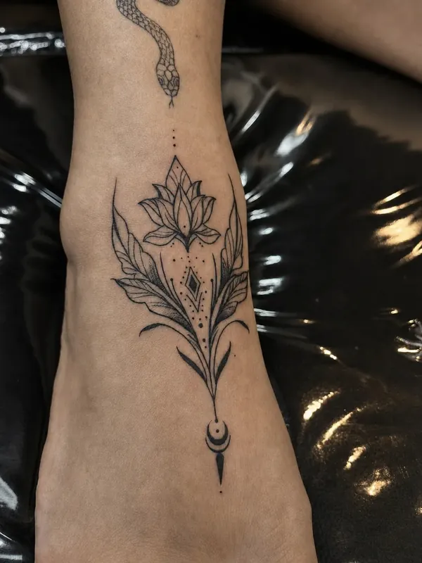 Tatuagem fine line de flor de lótus com folhas e pingente de lua no tornozelo