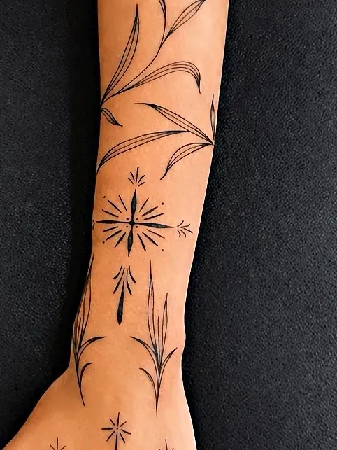 Tatuagem fine line de ramo com folhas descendo o antebraço até o dorso da mão, com estrelas